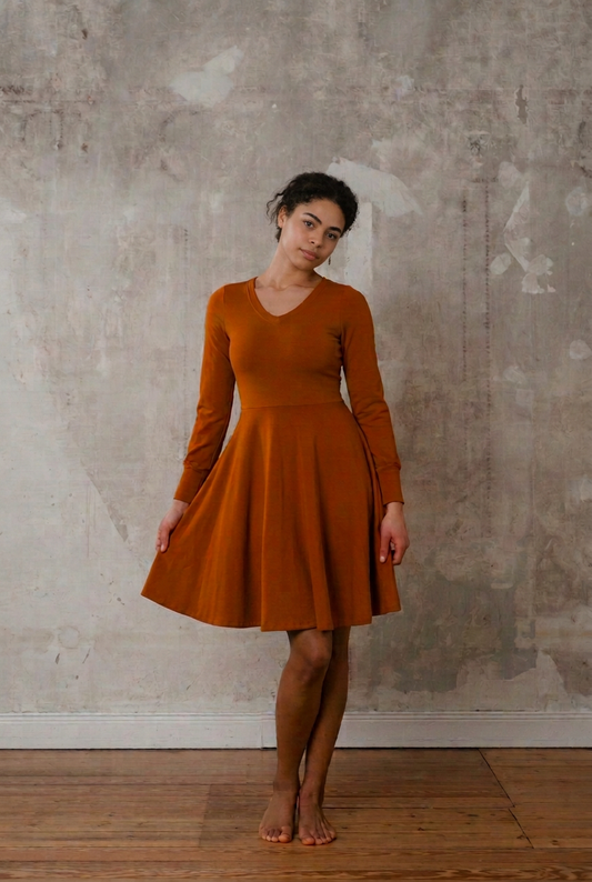 Sweatkleid Cinnamon in Rostrot mit V-Ausschnitt und langen Ärmeln, am Model mit leicht angehobenem Tellerrock